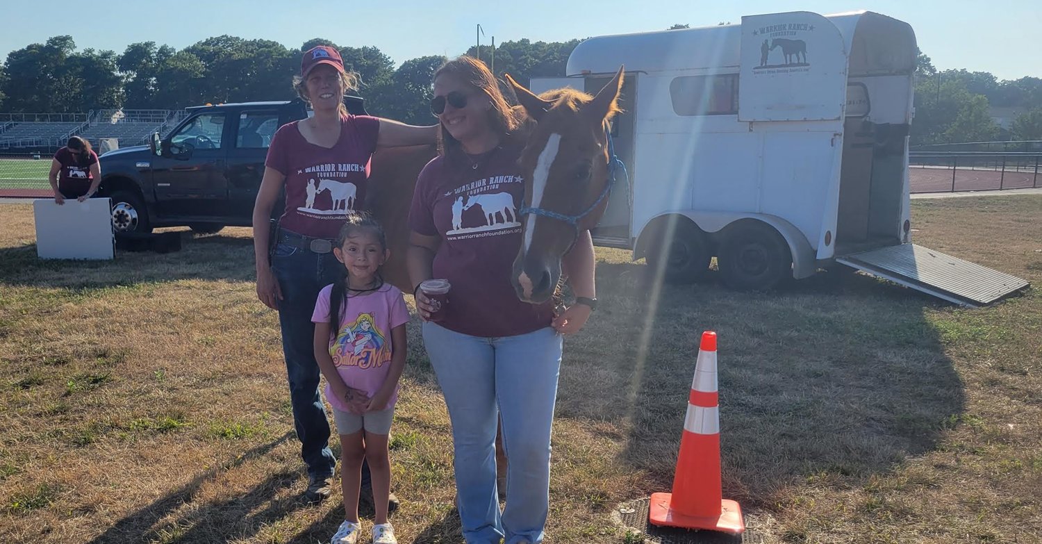 Eileen Shanahan, the founder and president of the Warrior Ranch Foundation (left), and Juliette Hackett, equine professional at the Warrior Ranch Foundation (right), introduce Alyssa Ruiz, a William Floyd Elementary School student, to a horse from the ranch.